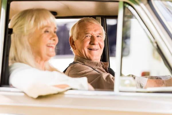 Vista laterale di sorridente anziano uomo e donna in auto d'epoca — Foto stock