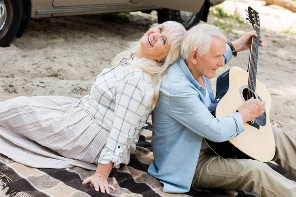 Mulher sênior sentado de volta para trás com o homem tocando guitarra na areia — Fotografia de Stock