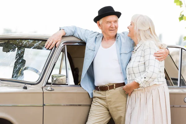 Стильная старшая пара, стоящая рядом с ретро-машиной и смотрящая друг на друга — стоковое фото