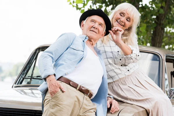 Homme âgé souriant près de la femme assise sur la voiture rétro beige — Photo de stock
