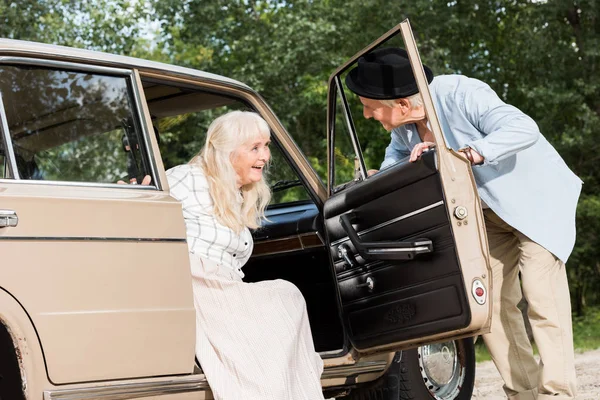 Senior man opening car door in front of beautiful woman — Stock Photo