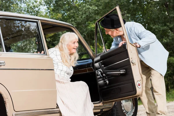 Hombre mayor abriendo la puerta del coche delante de la hermosa mujer - foto de stock