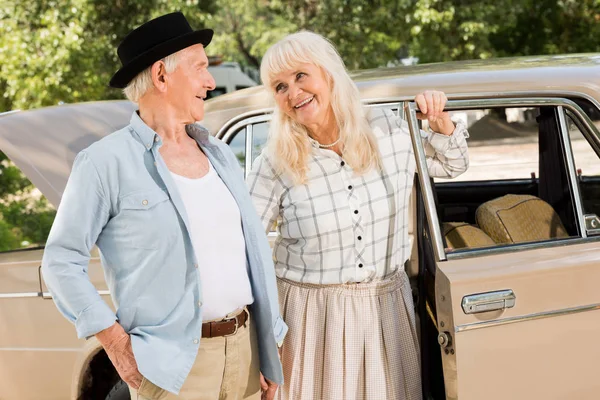 Beau couple de personnes âgées debout près de voiture beige et se regardant — Photo de stock