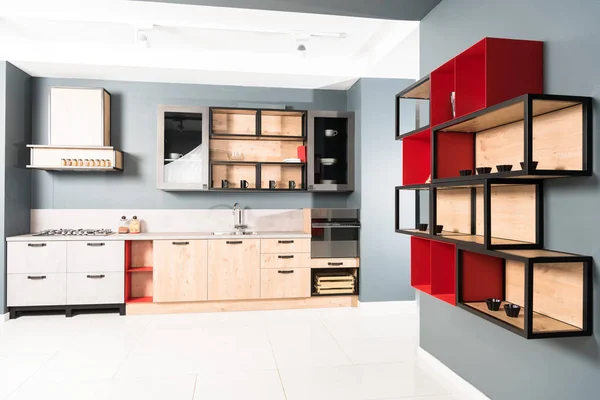 Интерьер современной чистой светлой кухни с мебелью и деревянными красными полками — стоковое фото