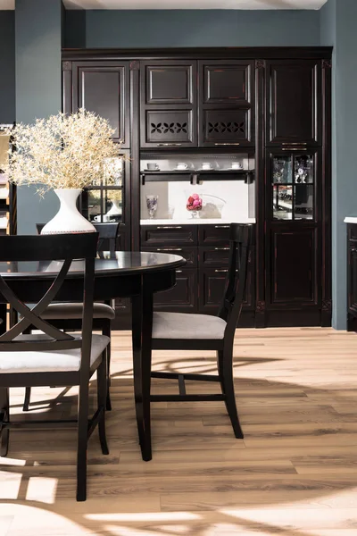 Interno della moderna sala da pranzo con mobili neri, vaso di fiori secchi sul tavolo e pavimento in legno — Foto stock