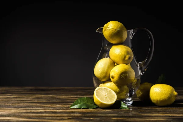 Glass jug with yellow lemons on wooden tabletop — Stock Photo
