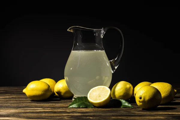 Brocca di vetro con succo biologico e limoni gialli intorno sul tavolo di legno — Foto stock