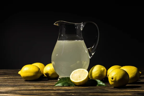 Jarro de vidro com suco orgânico e limões amarelos em torno de mesa de madeira — Fotografia de Stock