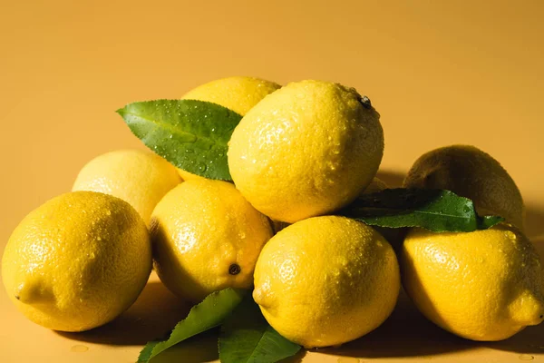 Limoni freschi bagnati con foglie su sfondo giallo — Foto stock