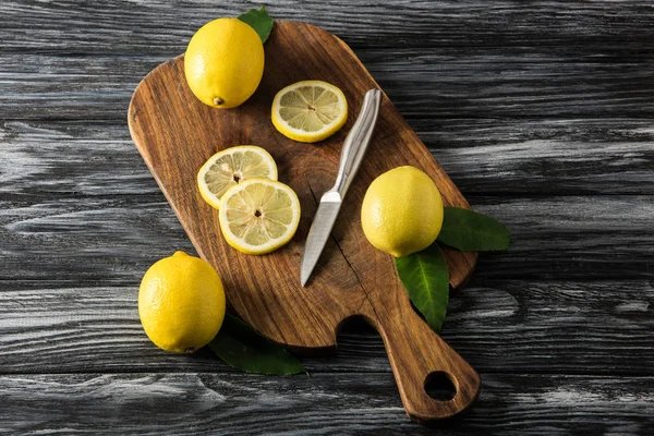 Juicy lemons and knife on cutting board on wooden table — Stock Photo