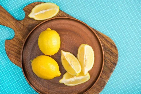 Top view of yellow lemons in ceramic plate on wooden cutting board on turquoise — Stock Photo