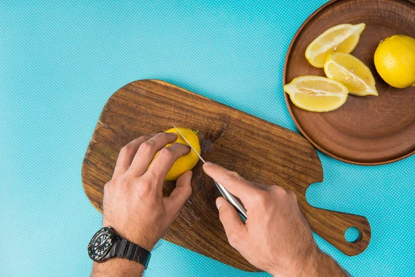 Vista recortada del hombre cortando limones amarillos en tablero de madera sobre fondo turquesa - foto de stock