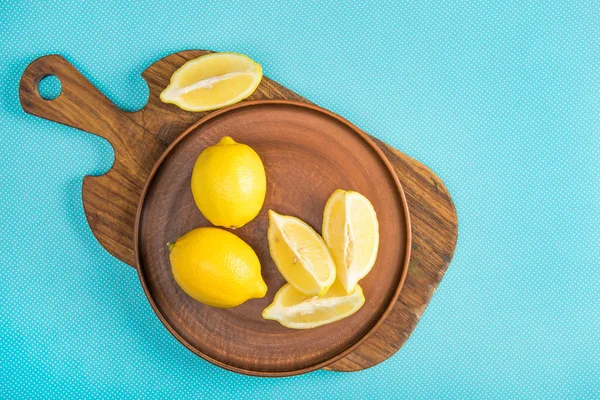Вид сверху на свежие лимоны в керамической пластине на деревянной доске для резки на бирюзовом фоне — стоковое фото