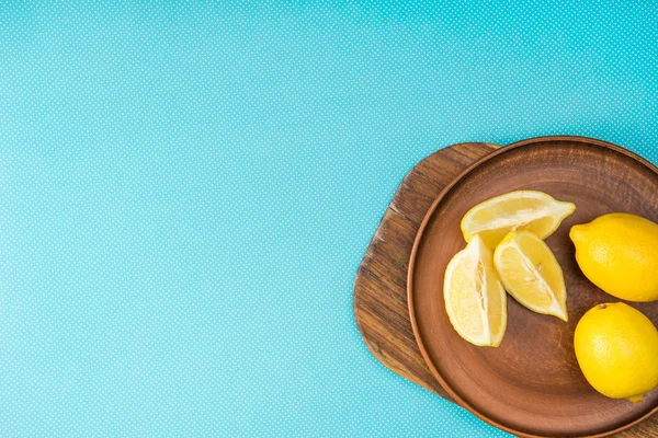 Vue du dessus des citrons dans une assiette en céramique sur une planche en bois turquoise avec espace de copie — Photo de stock