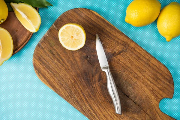 Top view of lemons and knife on wooden cutting board on turquoise background — Stock Photo