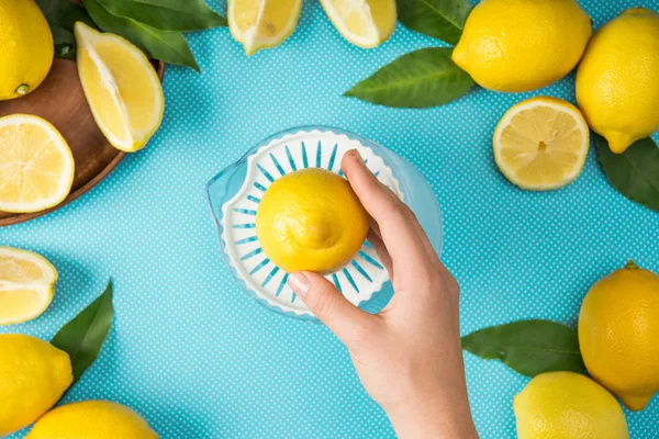 Vue de dessus de la main féminine avec citrons et pressoir sur fond turquoise — Photo de stock