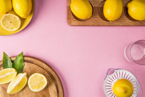 Вид на соковыжималку и свежие лимоны на деревянных досках на розовом фоне — стоковое фото