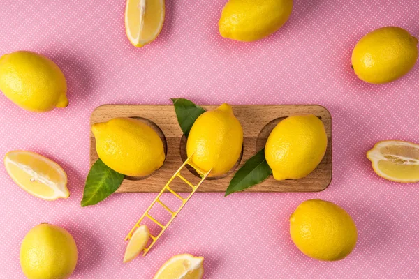 Vista superior de limones amarillos frescos sobre tabla de madera con pequeña escalera sobre fondo rosa - foto de stock