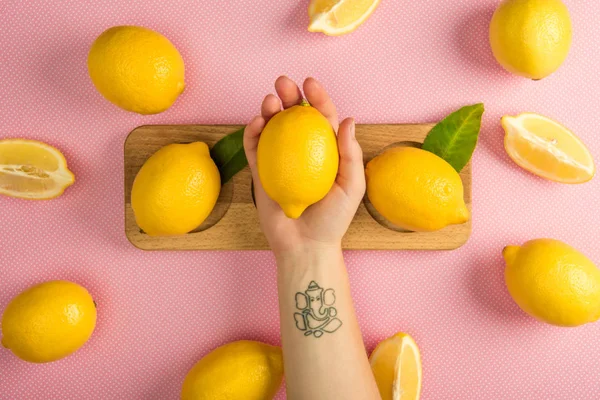 Vista cortada da mulher segurando limão amarelo sobre a mesa rosa com limões suculentos — Fotografia de Stock