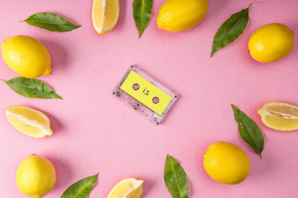 Вид зверху рамки з жовтих лимонів і листя з старовинною аудіокасетою всередині на рожевому — стокове фото