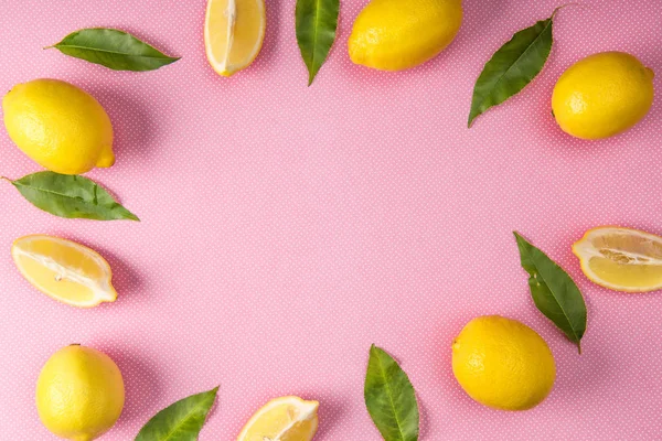 Vista superior del marco hecho de limones amarillos y hojas sobre fondo rosa con espacio para copiar - foto de stock