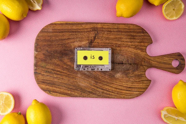 Top view of fresh lemons around cutting board with retro audio cassette on pink — Stock Photo
