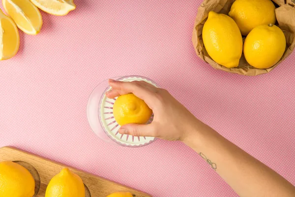 Vista recortada de la mujer exprimiendo jugo de limones sobre fondo rosa - foto de stock