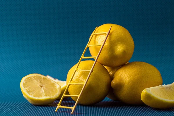 Fresh yellow lemons with little ladder on blue — Stock Photo