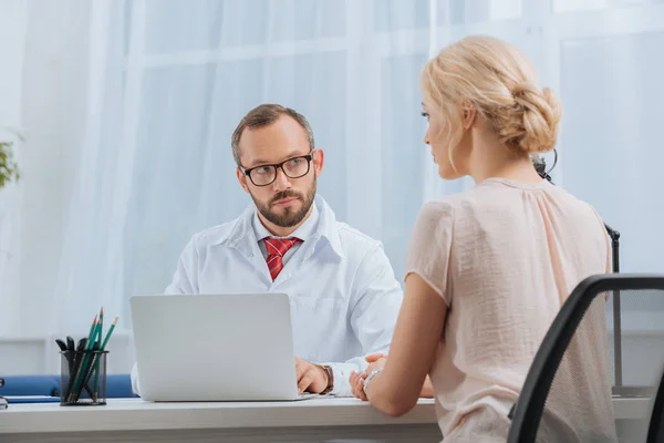 Physiotherapeutin im weißen Kittel im Gespräch mit Patientin am Arbeitsplatz mit Laptop im Krankenhaus — Stockfoto