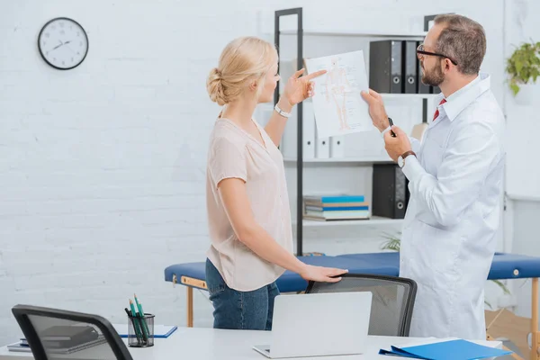 Quiropráctica en bata blanca que muestra esquema de cuerpo humano a paciente femenina en el hospital - foto de stock