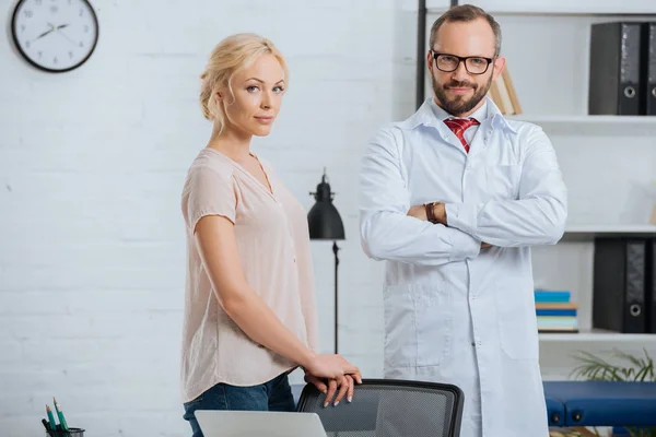Portrait of doctor in white coat and female patient looking at camera in clinic — Stock Photo
