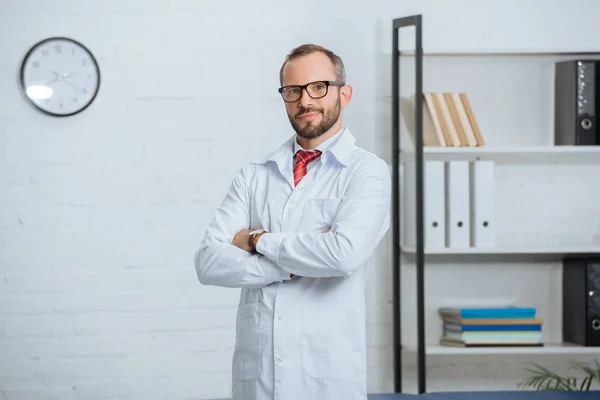 Portrait de chiropraticien masculin en manteau blanc et lunettes avec les bras croisés à l'hôpital — Photo de stock