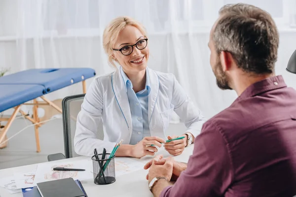 Smiling physiotherapist in white coat looking at patient during appointment in clinic — Stock Photo