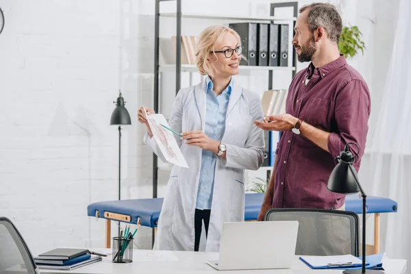 Fisioterapista femminile che mostra l'immagine del corpo umano al paziente in clinica — Foto stock