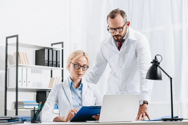 Portrait of physiotherapists in white coats and eyeglasses working together in clinic — Stock Photo