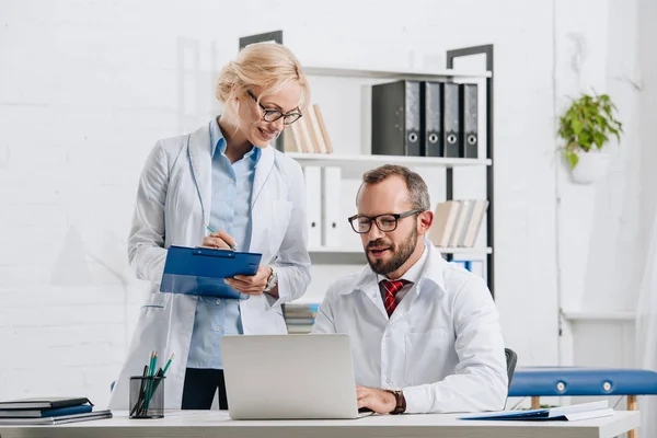 Portrait of physiotherapists in white coats and eyeglasses working together in clinic — Stock Photo