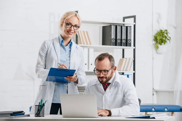 Portrait of physiotherapists in white coats and eyeglasses at workplace in clinic — Stock Photo