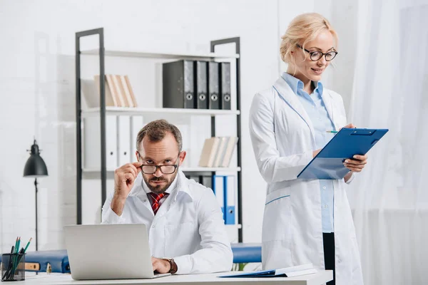 Portrait of physiotherapists in white coats and eyeglasses at workplace in clinic — Stock Photo