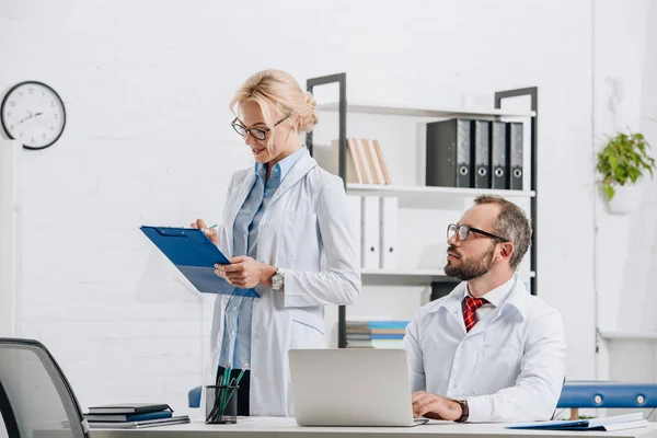 Portrait of physiotherapists in white coats and eyeglasses at workplace in clinic — Stock Photo