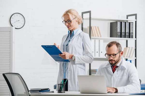 Portrait of physiotherapists in white coats and eyeglasses at workplace in clinic — Stock Photo