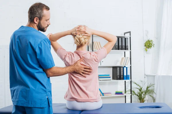 Vista posterior del fisioterapeuta haciendo masaje a la mujer en la mesa de masaje en el hospital - foto de stock