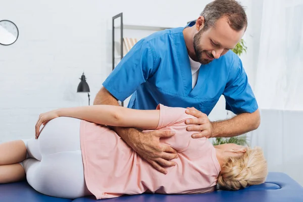 Portrait of smiling chiropractor massaging back of patient that lying on massage table in hospital — Stock Photo