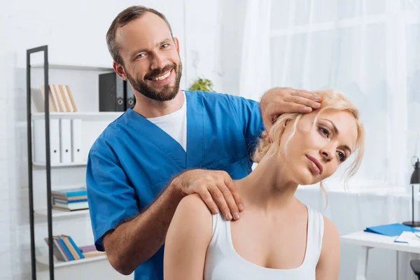 Porträt eines lächelnden Chiropraktikers, der Frau während eines Krankenhausaufenthalts den Hals streckt — Stockfoto