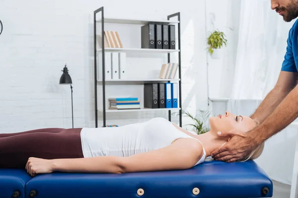 Частичный вид физиотерапевта массирующего шею пациента, лежащего на массажном столе в клинике — стоковое фото