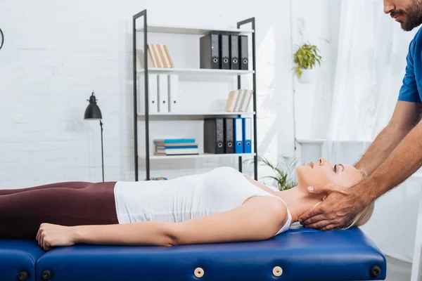 Vista parcial del fisioterapeuta masajeando cuello de paciente que yace sobre mesa de masaje en clínica - foto de stock