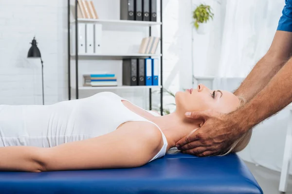 Частичный вид физиотерапевта массирующего шею пациента, лежащего на массажном столе в клинике — стоковое фото