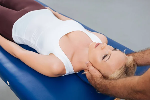 Partial view of physiotherapist massaging neck of patient that lying on massage table in clinic — Stock Photo