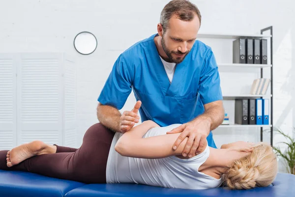 Partial view of physiotherapist stretching patient on massage table in hospital — Stock Photo