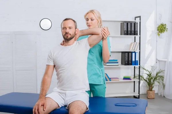 Retrato del fisioterapeuta estirando el brazo del hombre en el hospital - foto de stock