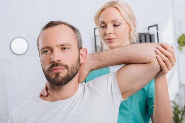 Portrait of physiotherapist stretching mans arm in hospital — Stock Photo